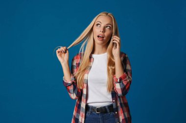 Güzel sarışın bir kızın mavi arka planda izole bir şekilde akıllı telefondan konuştuğunu düşünüyorum.