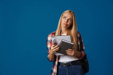 Düşünceli sarışın beyaz kız elinde belgelerle poz veriyor ve planlamacı mavi arka planda izole edilmiş.