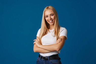 Sarışın, genç, mutlu kadın gülümseyen ve mavi arka planda izole edilmiş kameraya bakan.