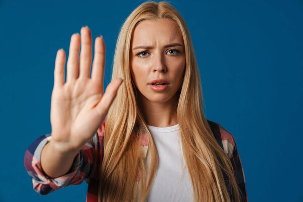 Blonde young displeased woman showing stop gesture at camera isolated over blue background