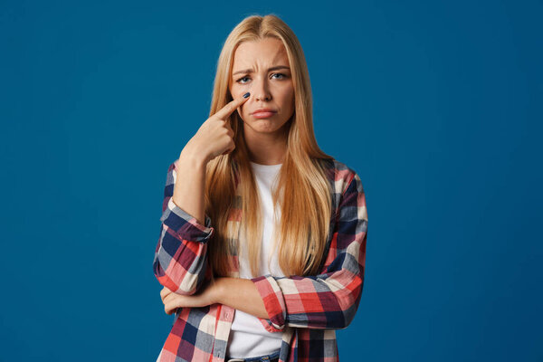 Blonde young upset woman crying and looking at camera isolated over blue background