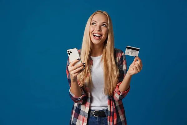 ブロンド励起女性使用携帯電話と示すクレジットカード絶縁以上青の背景 — ストック写真