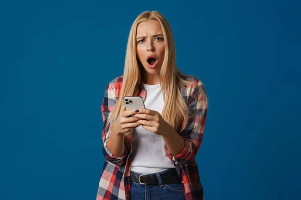 Ξανθιά Λευκή Σοκαρισμένη Γυναίκα Αναφωνώντας Χρησιμοποιώντας Κινητό Τηλέφωνο Απομονωμένο Μπλε — Φωτογραφία Αρχείου