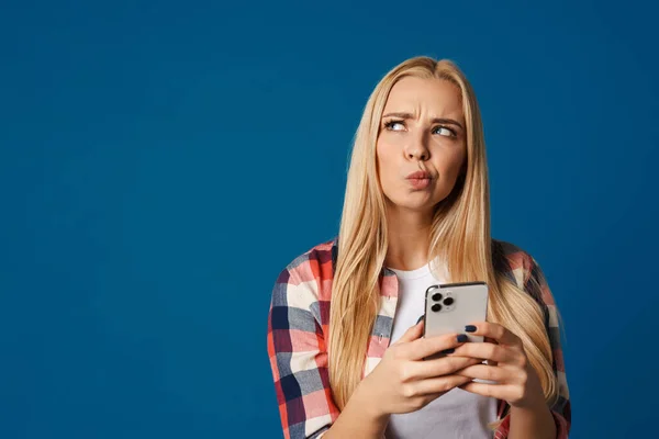 Mujer Rubia Desconcertada Mirando Lado Mientras Utiliza Teléfono Móvil Aislado — Foto de Stock