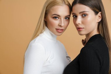 Tepeden tırnağa poz veren güzel iki kadın izole edilmiş bej arka planda.