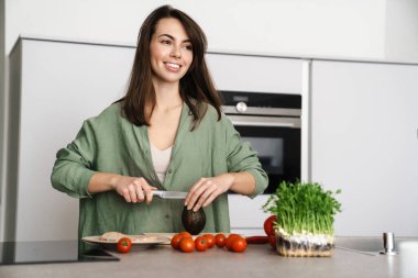 Mutfakta avokadoyla salata yaparken gülümseyen mutlu güzel kadın.