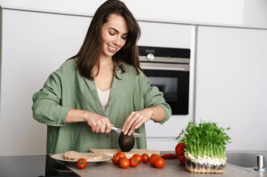 Mutfakta avokadoyla salata yaparken gülümseyen mutlu güzel kadın.