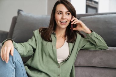Neşeli, güzel bir kadın evde otururken cep telefonuyla konuşuyor.