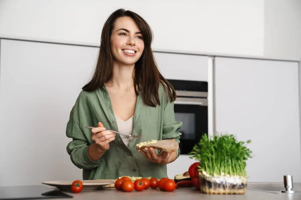 Fröhliche Brünette Frau Lächelt Während Sie Der Heimischen Küche Sandwich — Stockfoto