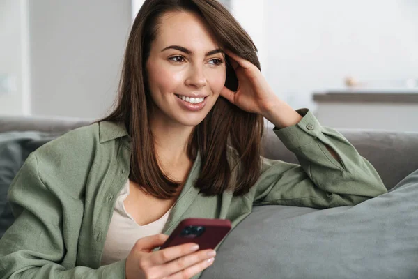 Glückliche Brünette Frau Lächelt Und Benutzt Handy Während Sie Hause — Stockfoto