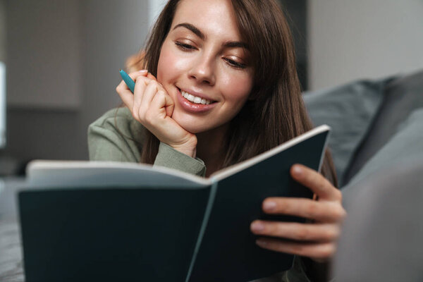 Smiling woman laying on couch and writing in a diary