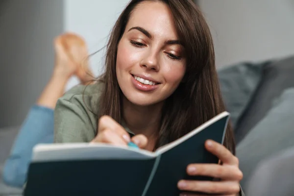 Joven Mujer Sonriente Escribiendo Notas Mientras Está Acostada Sofá Casa — Foto de Stock