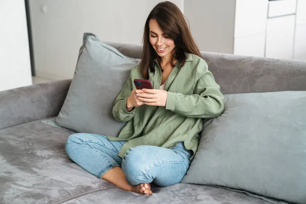 Sorrindo Mulher Atraente Usando Telefone Celular Enquanto Sentado Sofá Casa — Fotografia de Stock