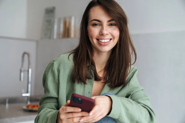 Fiatal Mosolygós Mobiltelefont Használ Miközben Otthon Konyhában — Stock Fotó