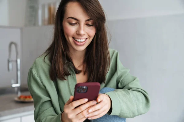 Junge Lächelnde Frau Benutzt Handy Während Sie Hause Der Küche — Stockfoto