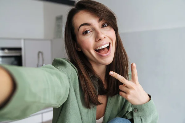 Молодая Счастливая Женщина Показывает Знак Мира Делая Селфи Фото Домашней — стоковое фото