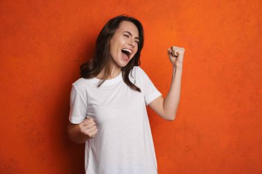 Heyecanlı güzel kız çığlık atıyor ve gri duvarda izole edilmiş kazanan jestler yapıyor.