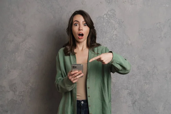Shocked Beautiful Girl Holding Pointing Finger Cellphone Isolated Grey Wall — Stock Photo, Image