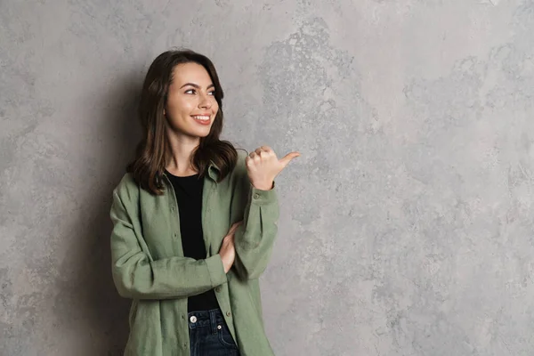 Gelukkig Mooi Brunette Meisje Glimlachen Wijzend Vinger Opzij Geïsoleerd Grijze — Stockfoto