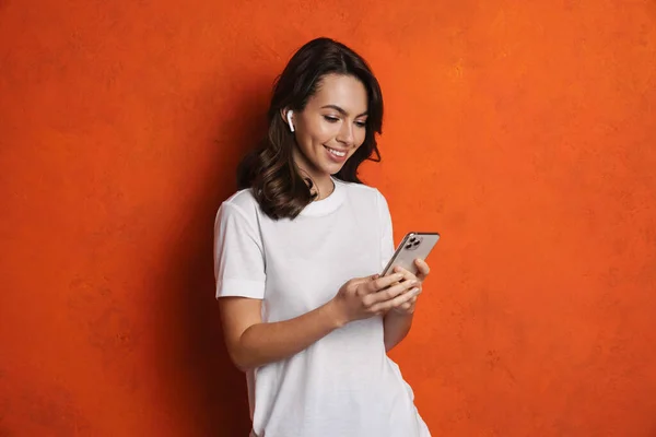 Glad Flicka Hörlurar Ler När Använder Mobiltelefon Isolerad Över Orange — Stockfoto