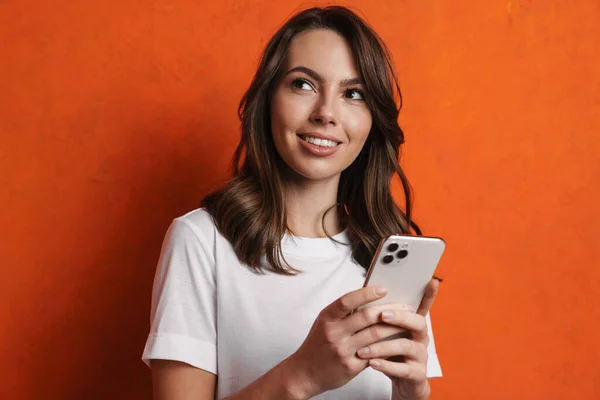 快乐迷人的女孩微笑着 用隔离在橙色墙壁上的手机 — 图库照片
