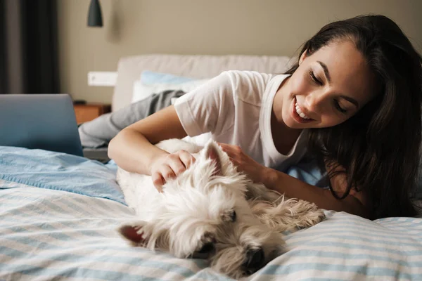 Mutlu beyaz kadın evde yatarken köpeğini okşuyor.