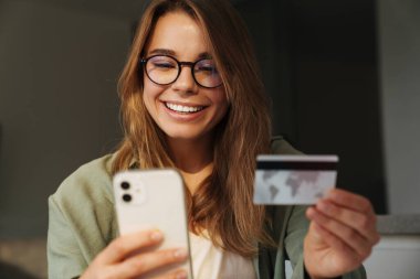 Cep telefonu ve kredi kartı kullanırken gülümseyen güzel bir kadın.