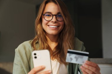 Cep telefonu ve kredi kartı kullanırken gülümseyen güzel bir kadın.