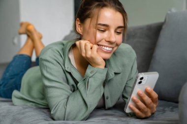 Evdeki koltukta uzanırken cep telefonu kullanan mutlu bir kadın.