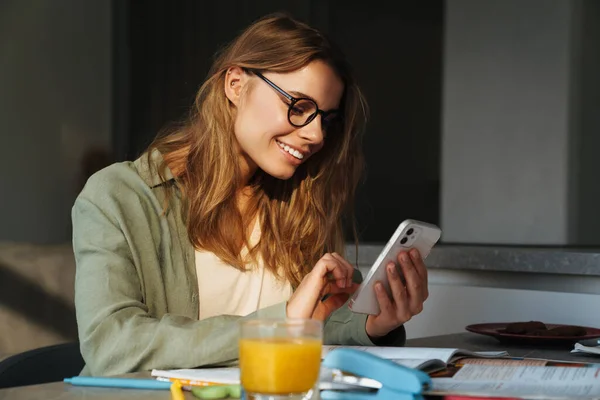 Feliz Estudiante Agradable Mujer Usando Teléfono Móvil Mientras Hace Tarea — Foto de Stock