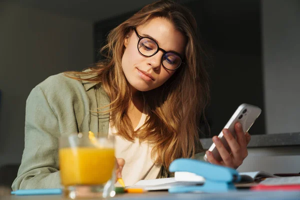 Enfocado Agradable Estudiante Mujer Usando Teléfono Móvil Mientras Hace Tarea — Foto de Stock