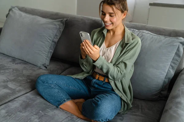 Feliz Mulher Agradável Usando Telefone Celular Enquanto Sentado Sofá Casa — Fotografia de Stock