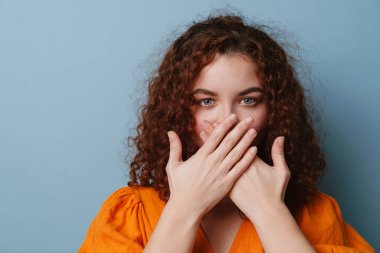 Kızıl saçlı kıvırcık kız kameraya bakıyor ve güvesini mavi arka planda gizliyor.