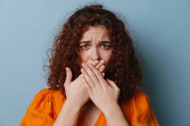 Mutsuz kızıl kadın yüzünü buruşturuyor ve mavi arka planda ağzını kapatıyor.