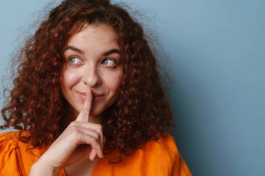 Mutlu kızıl kadın gülümserken mavi arka planda izole edilmiş sessizlik hareketi gösteriyor.