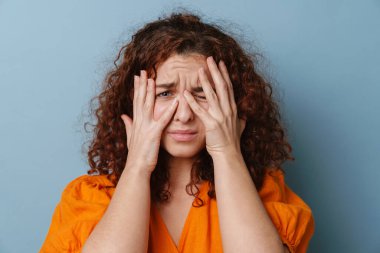 Mutsuz kızıl kadın yüzünü buruşturuyor ve mavi arka planda soyutlanıyor.