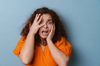 Korkmuş kızıl kadın yüzünü buruşturuyor ve mavi arka planda soyutlanıyor.