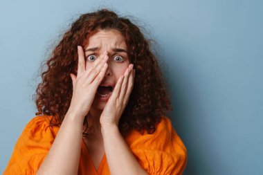 Korkmuş kızıl kadın yüzünü buruşturuyor ve mavi arka planda soyutlanıyor.