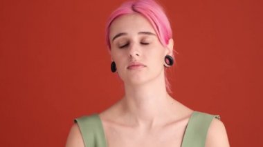 Pembe saçlı üzgün genç bir kadın, atölyedeki turuncu duvarın üzerinde gözlerinden yaşlar süzülüyor.