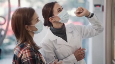 Koruyucu tıbbi maske takan profesyonel bir eczacı kadın eczanedeki bir müşteriye danışıyor.