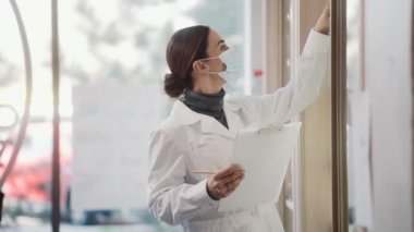 Koruyucu tıbbi maske takan odaklanmış bir kadının yan görünüşü, sağlanan ve modern bir eczanede envanter sayımı yapan bir şey yazıyor.