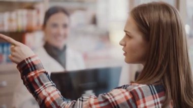 Eczanede çalışan bir müşterinin, eczacıyla konuşurken eczane raflarını göstermesinin arkası.