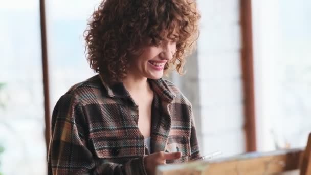 Beautiful Curly Woman Artist Using Her Smartphone Sitting Her Art — Stock Video