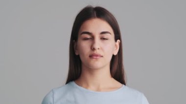 Güzel bir genç kadın kameraya bakıyor. Stüdyoda gri duvarın üzerinde tek başına duruyor.