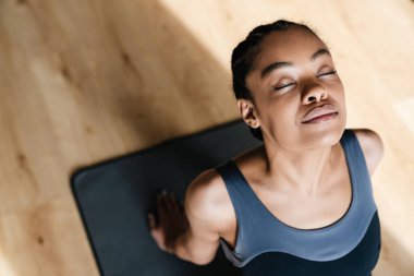 Top view of beautiful young african woman in sportswear practicing yoga while sitting on the floor