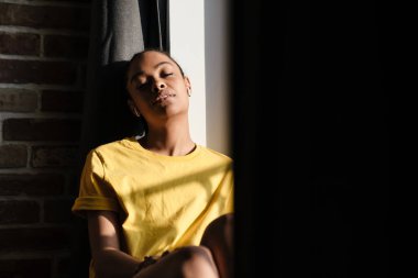 Rahatlamış Afro-Amerikalı kız evde otururken kulaklıkla müzik dinliyor.