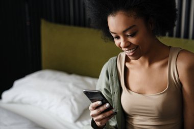 Mutlu Afro-Amerikan kızı evde uyuduktan sonra yatakta cep telefonu kullanıyor.