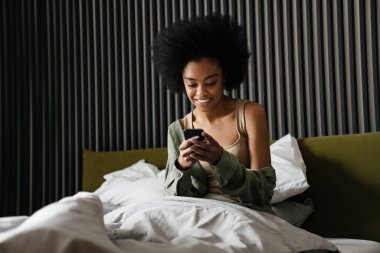 Mutlu Afro-Amerikan kızı evde uyuduktan sonra yatakta cep telefonu kullanıyor.