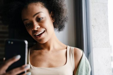 Orta yaşlı mutlu bir Afrikalı kadın cep telefonuyla resim çekiyor.