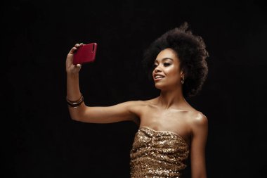 Mutlu Afrikalı Amerikalı kadın siyah arka planda izole edilmiş cep telefonuyla selfie çekiyor.